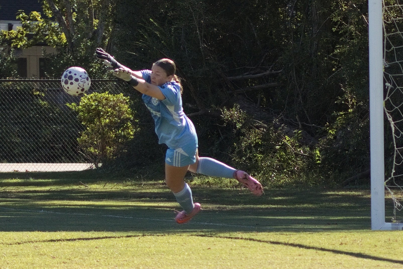 Goalkeeper fully airborne, getting both gloves to the ball for a diving save
