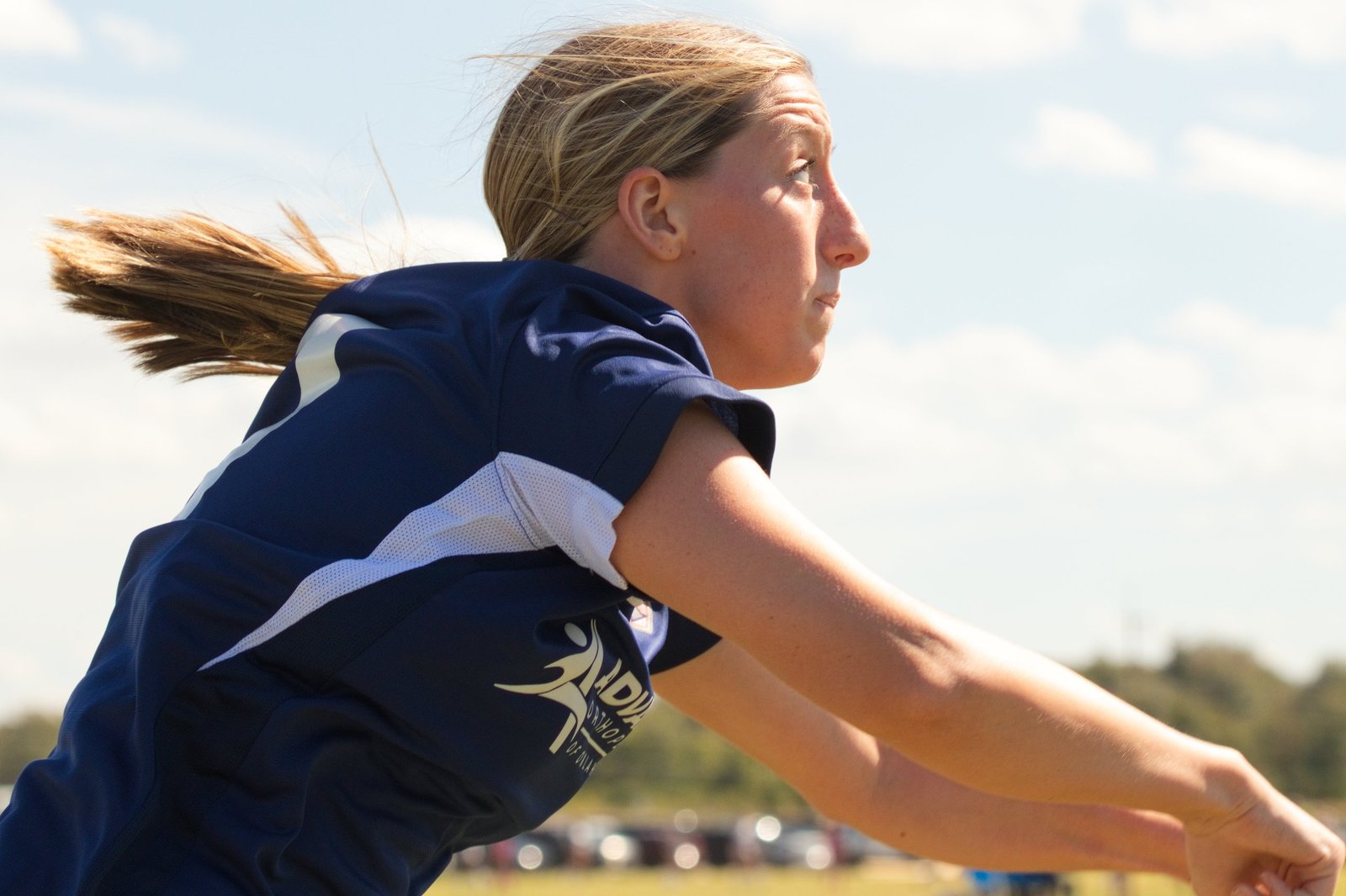 Soccer player with her ponytail flying, eyes locked on the field as she releases a throw