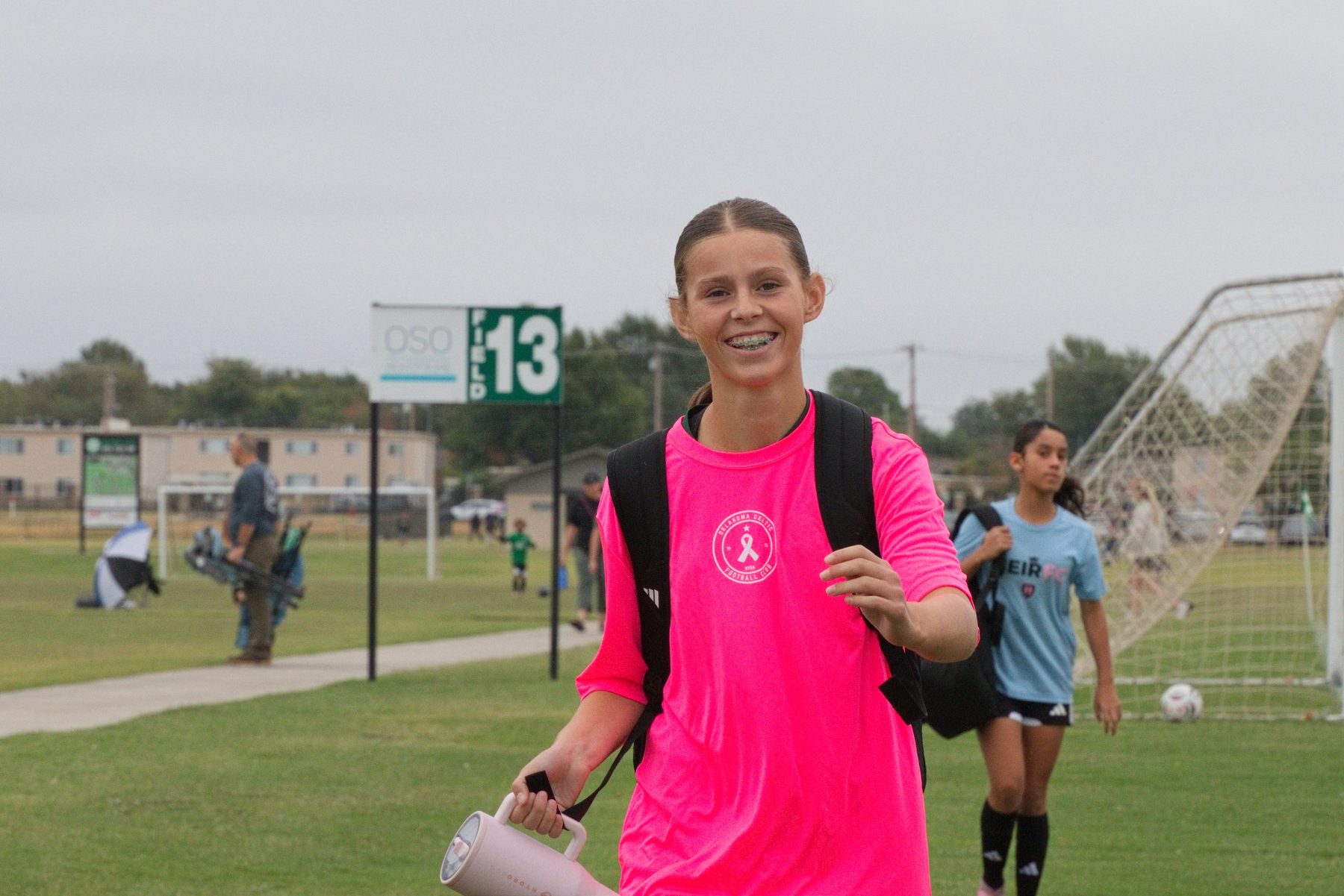 Smiling soccer player in a pink shirt walking off the field with her gear