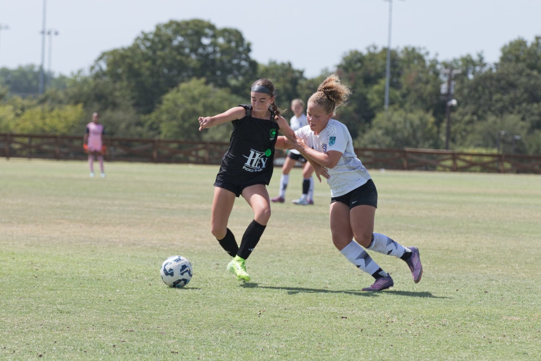 Soccer player pushing the ball ahead while a defender grabs at her